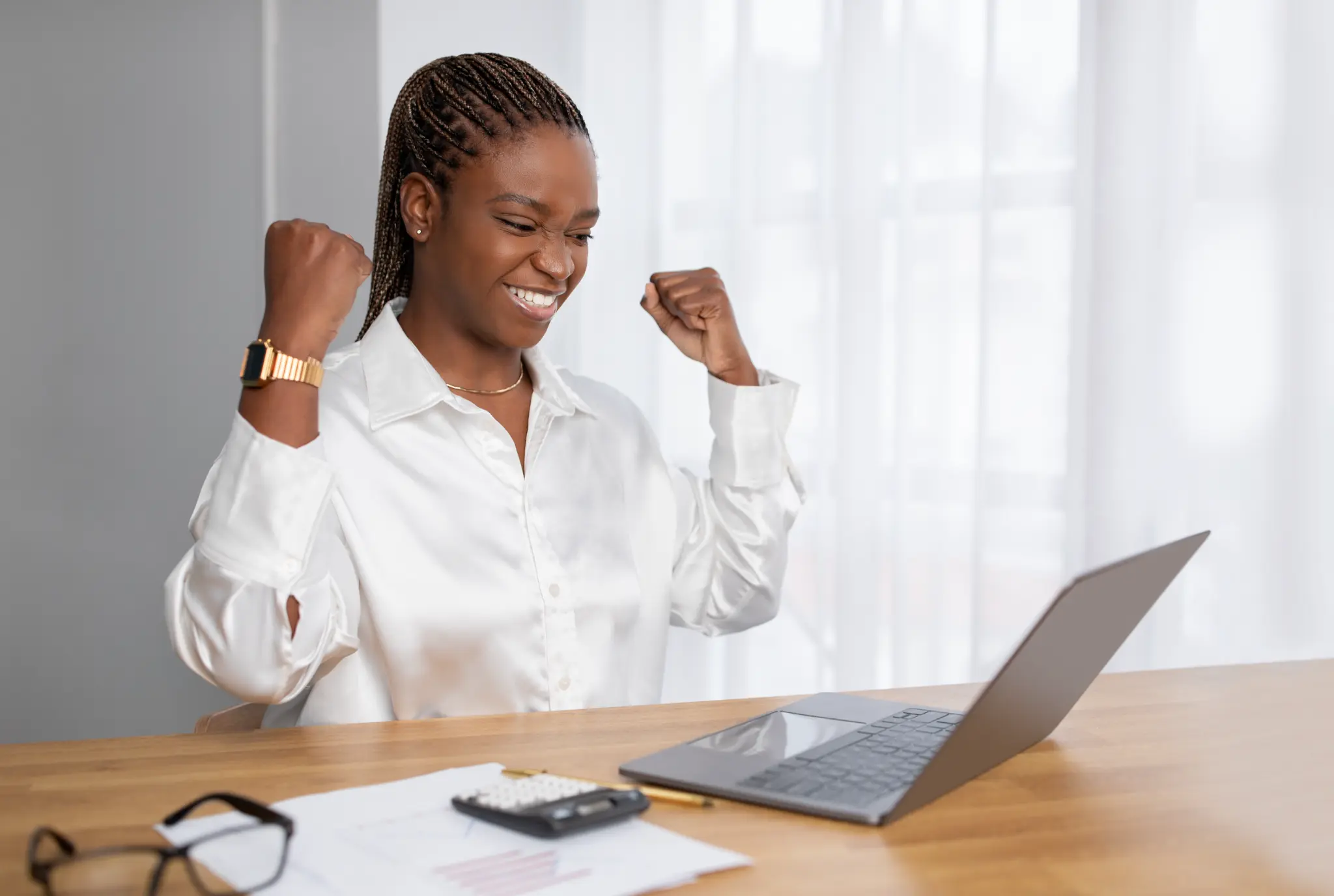 Woman celebrating a success at her desk beside an open laptop